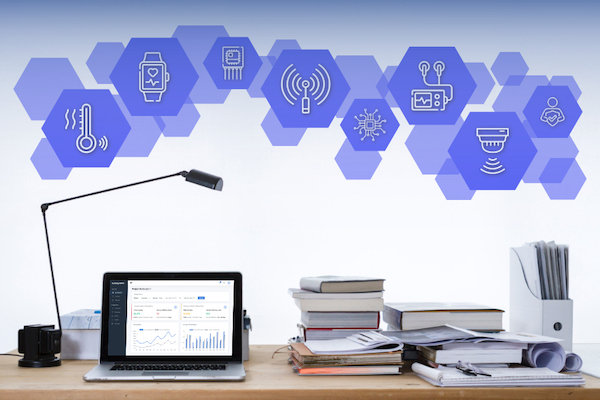 A desk with books, papers, a laptop displaying the ObserveKit dashboard surrounded by icons of sensors and devices.